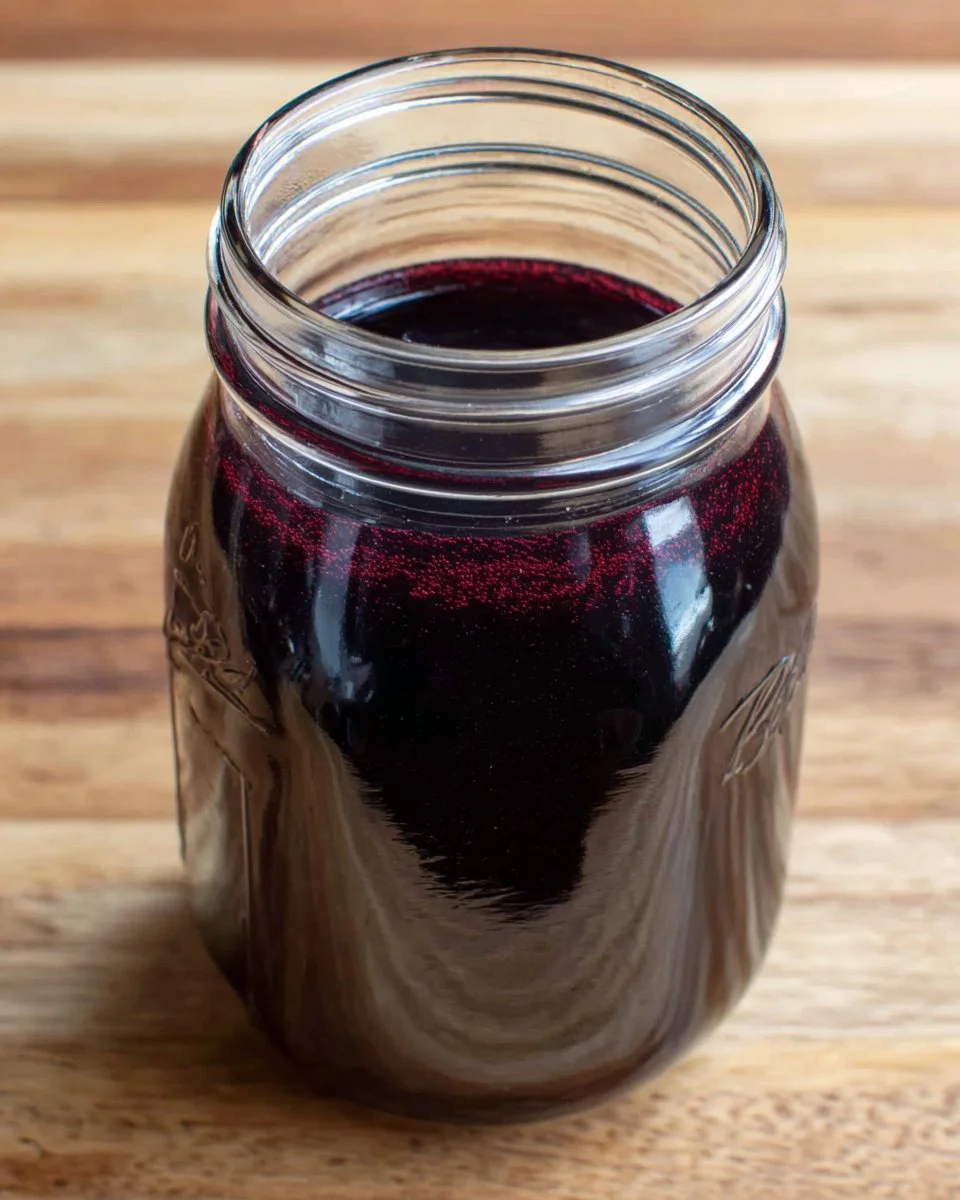 Homemade blueberry simple syrup served in a glass jar on a wooden table